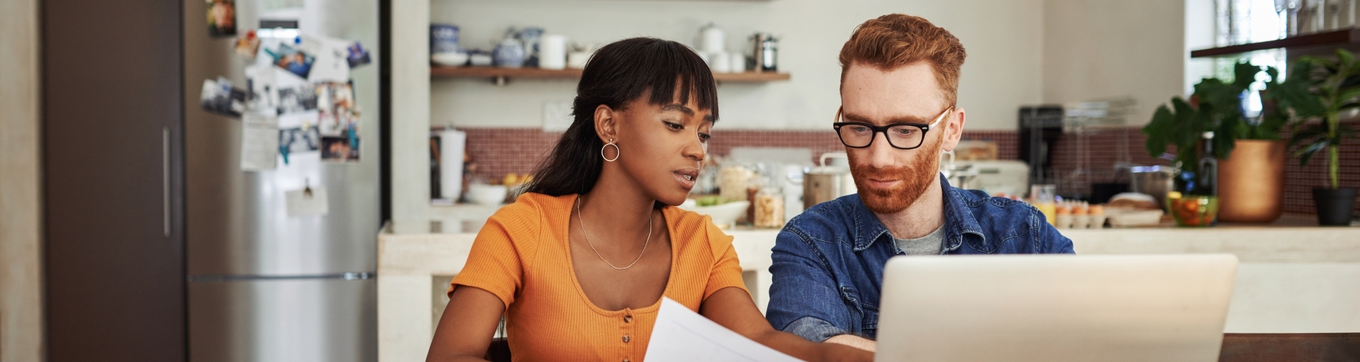 Image of couple sitting at their dinning room table and looking at paperwork and laptop